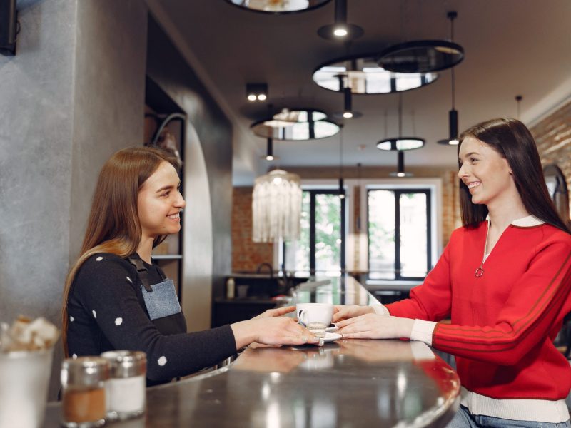 Female barista preparing coffee at coffee shop. Worker talking with a costumer. The concept of restaurant business and quality of service.