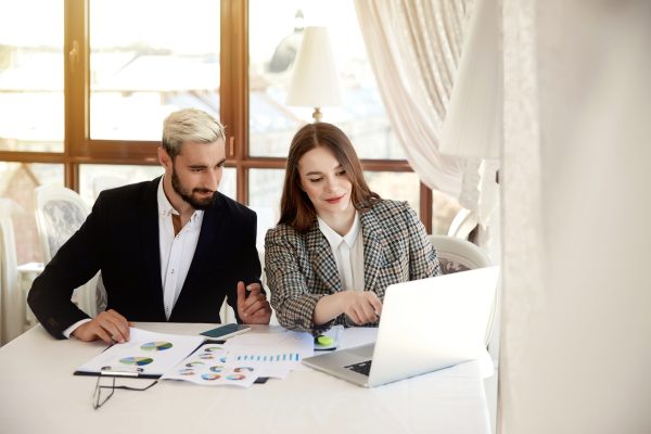 Young blonde man and brunette woman are looking at the computer and discussing business plans